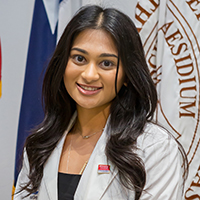 Woman with long, wavy dark hair wearing a black shirt and white coat